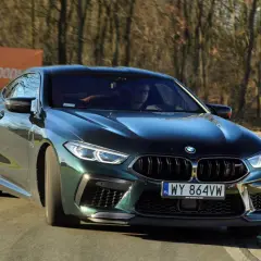 Mocne m8 bmw w ciemnozielonym kolorze na torze wyścigowym, z widocznym banerem "TOR MODLIN" w tle.