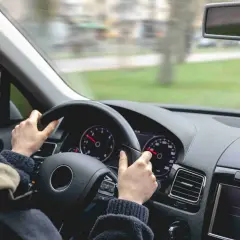 Kobieta prowadzi samochód, trzymając kierownicę. Widok z wnętrza pojazdu, gdzie panuje ruch lewostronny.
