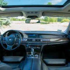 Wnętrze BMW 7 F01 z widokiem na otwartą przestrzeń i niebo. Skórzana tapicerka, drewniane wykończenia i nowoczesny kokpit.