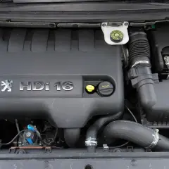 Silnik 1.6 HDI w Peugeot 307. Widoczna pokrywa silnika z logo i oznaczeniem, zbiornik płynu hamulcowego, filtr powietrza i akumulator.
