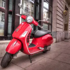 Czerwona Vespa, idealna do miejskiej kategoria am czym można jeździć. Stylowy pojazd na brukowanym chodniku.