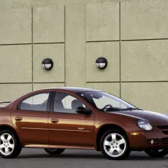 Brązowy Dodge Neon R/T z 2004 roku stoi przed betonową ścianą z dwoma okrągłymi lampami.