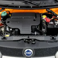 Silnik 1.3 Multijet w samochodzie Fiat. Widoczny akumulator, zbiornik płynu chłodniczego i osłona silnika.