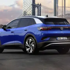 Niebieski Volkswagen ID.4 z białym dachem, zaparkowany na tle miasta z mostem i nowoczesnymi budynkami.