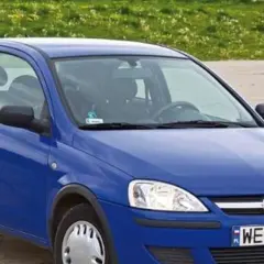 Niebieski Opel Corsa C 1.2 z tablicą WE 3063F stoi na tle zielonej łąki.