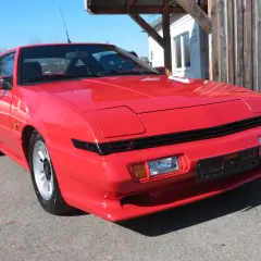 Czerwony Mitsubishi Starion z lat 80. błyszczy w słońcu. Klasyk sportowy z wysuwanymi światłami.