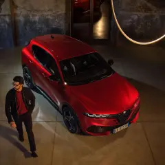 Elegancki mężczyzna w okularach obok lśniącego, czerwonego Alfa Romeo Tonale. Sprawdź aktualną alfa romeo tonale cena i odkryj jego styl.