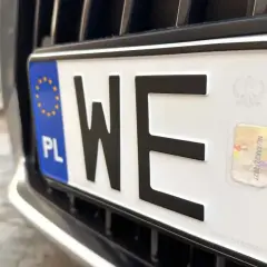 Zbliżenie na polską tablicę rejestracyjną z literami "WE". Widoczny symbol Unii Europejskiej i hologram.