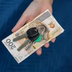 Dłoń trzyma banknot 200 zł i klucze. Symbolizuje to zsl rejestracja, np. kupno samochodu.