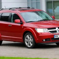 Czerwony Dodge Journey 3.6 z relingami dachowymi jedzie po brukowanej drodze.