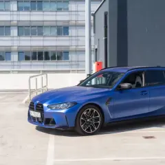 Niebieskie BMW G81 na parkingu, z nowoczesnym budynkiem w tle.