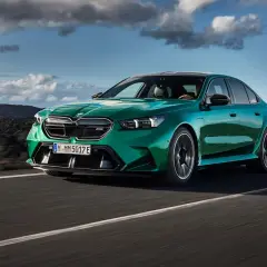 Zielony BMW M5 na drodze, chmury na niebie. Sprawdź aktualną bmw m5 cena i możliwości tego sportowego sedana.