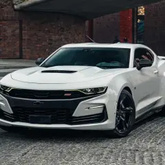Biały Chevrolet Camaro SS z czarnymi felgami stoi na brukowanej ulicy przed ceglanym budynkiem.