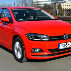 Czerwony Volkswagen Polo 6 w ruchu miejskim. Kierowca w okularach przeciwsłonecznych prowadzi auto po ulicy.