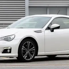 Białe Toyota BRZ z czarnymi felgami stoi przed budynkiem z poziomymi żaluzjami.