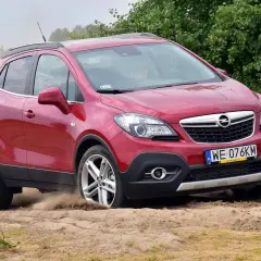 Czerwony Opel Mokka 1.4 Turbo z napędem na cztery koła pokonuje piaszczysty teren, wzbijając tumany kurzu.