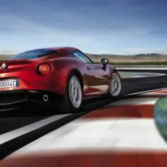 Czerwone Alfa Romeo 4C na torze wyścigowym, z rozmytymi kołami i kolorowymi bandami.