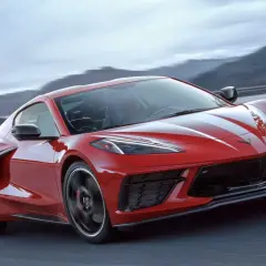 Czerwony Chevrolet Corvette C8 z białymi pasami pędzi po krętej drodze wśród gór.