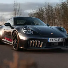 Czarny Porsche GTS z czerwonymi akcentami na progu, zaparkowany na drodze wśród suchych traw.
