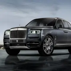 Elegancki Rolls-Royce SUV w ciemnym kolorze, lśniącym na tle nocnego miasta i gór.