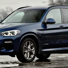 Ciemnoniebieskie BMW X3 na mokrej nawierzchni. Eleganckie linie i sportowy charakter tego SUV-a robią wrażenie.