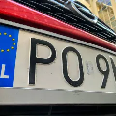 Czerwony samochód z polską tablicą rejestracyjną PO 9MH0. Widoczny fragment grilla i logo marki.