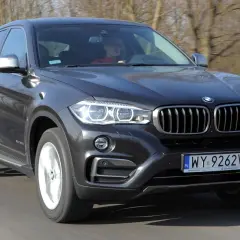 Ciemnoszary BMW F16 w ruchu drogowym, z kierowcą za kierownicą.