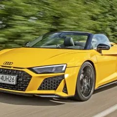 Żółty kabriolet Audi R8 V10 pędzi po drodze, otoczony rozmytymi zielonymi drzewami.