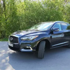 Ciemny Infiniti QX60 zaparkowany na poboczu drogi, otoczony zielenią drzew.