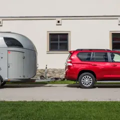 Czerwony SUV holuje przyczepę kempingową z rysunkiem konia. Idealny zestaw dla posiadaczy prawa jazdy na przyczepę.