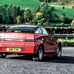 Czerwone Alfa Romeo SZ z czarnym dachem i spoilerem jedzie po wiejskiej drodze.