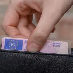 Dłoń wkłada do czarnego portfela polskie prawo jazdy kategorii B.
