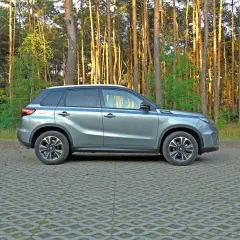 Nowy Suzuki Vitara 2025 w szarym kolorze, zaparkowany na tle sosnowego lasu.