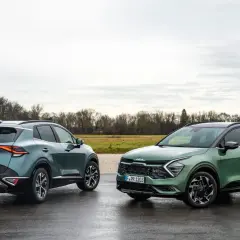 Dwa nowe Kia Sportage GT Line w zielonych odcieniach stoją na mokrej drodze.