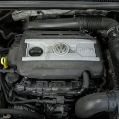 Silnik 2.0 TSI Volkswagena, widok z góry. Widać pokrywę silnika z logo VW i napisem TSI, elementy układu dolotowego i chłodzenia.