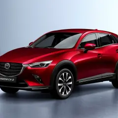 Czerwona Mazda CX-3 na tle jasnoszarego tła. Stylowy crossover, który zbiera pozytywne mazda cx-3 opinie.