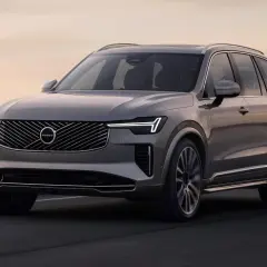 Elegancki, szary Volvo CX90 jedzie po drodze nad morzem o zachodzie słońca.