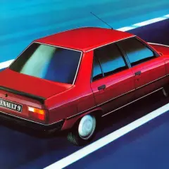 Czerwony Renault 9 sunie po drodze, odbijając niebieskie niebo w szybach.