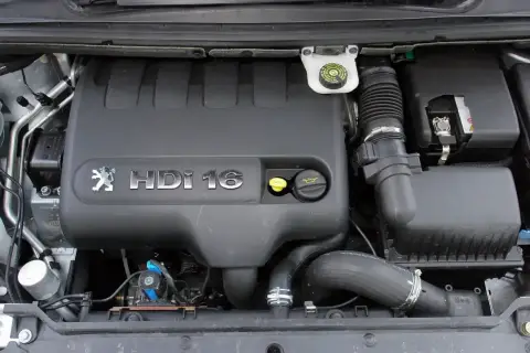 Silnik 1.6 HDI w Peugeot 307. Widoczna pokrywa silnika z logo i oznaczeniem, zbiornik płynu hamulcowego, filtr powietrza i akumulator.