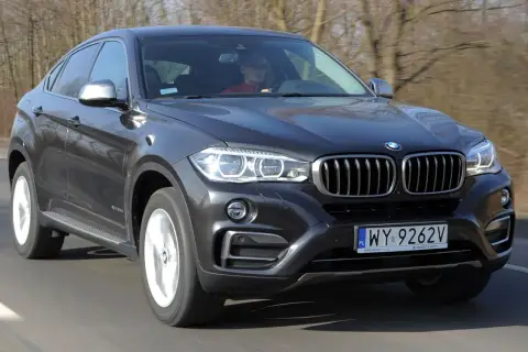 Ciemnoszary BMW F16 w ruchu drogowym, z kierowcą za kierownicą.
