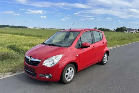 Czerwony Opel Agila 1.2 na tle zielonych pól i błękitnego nieba.