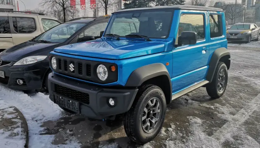 Niebieski Suzuki Jimny 2026 gotowy na zimowe przygody, zaparkowany na śniegu obok innych samochodów.