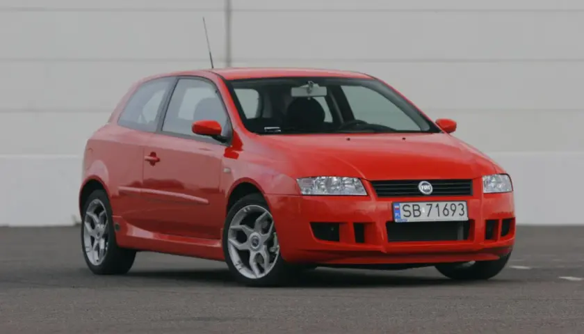 Czerwony Fiat Stilo 1.9 JTD na tle białej ściany, gotowy do jazdy.