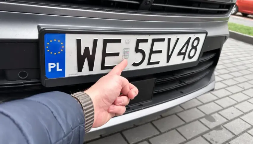 Palec wskazuje hologram na tablicy rejestracyjnej WE 5EV48, świeżo po rejestracji samochodu.