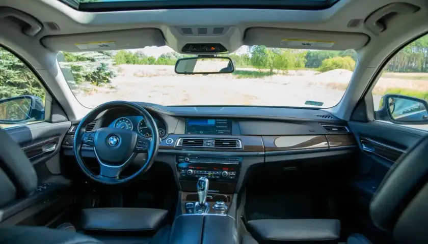 Wnętrze BMW 7 F01 z widokiem na otwartą przestrzeń i niebo. Skórzana tapicerka, drewniane wykończenia i nowoczesny kokpit.