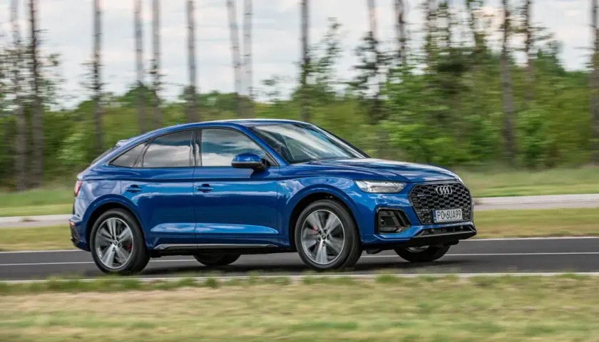 Błękitny Audi Q5 Sportback 2025 w ruchu, z rozmytym tłem lasu. Dynamiczna sylwetka i sportowy charakter.