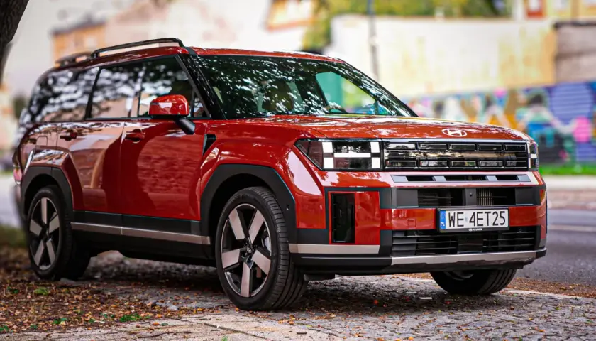 Czerwony Hyundai Santa Fe 2025 z charakterystycznym przednim grillem i światłami, zaparkowany na brukowanej ulicy.
