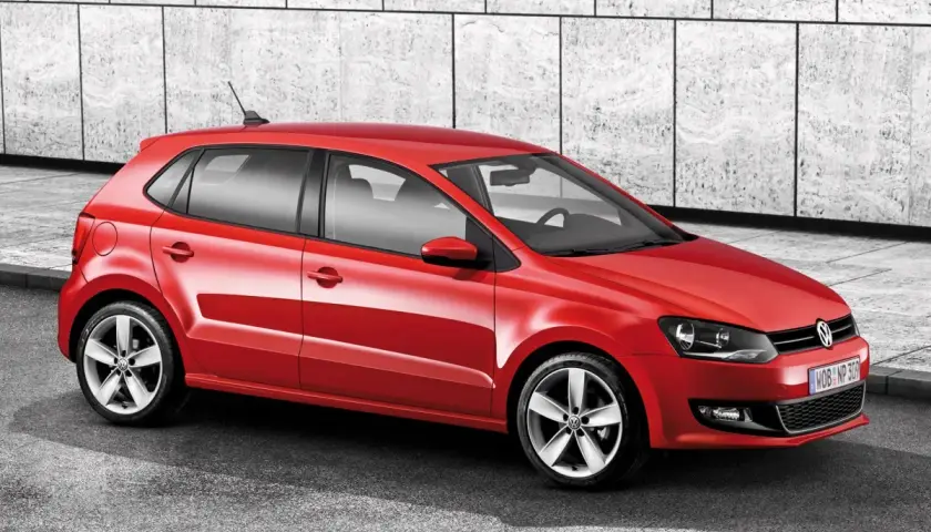 Czerwony Volkswagen Polo 6R z felgami aluminiowymi stoi na tle nowoczesnej, betonowej ściany.