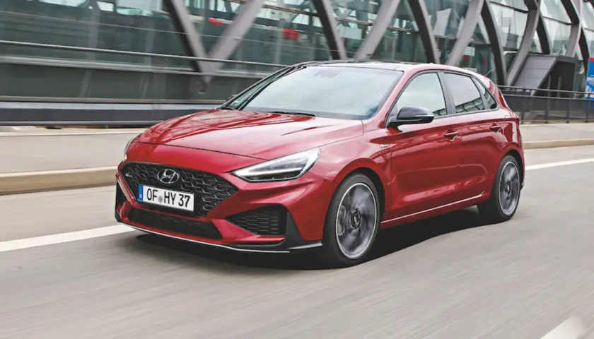 Czerwony Hyundai i30 2024 w wersji N Line pędzi po drodze, z nowoczesną atrapą chłodnicy i ostrymi światłami LED.