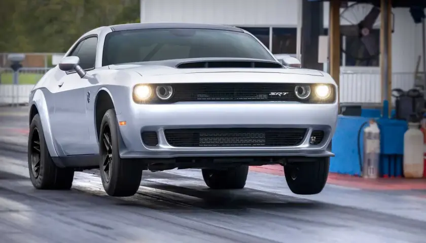 Srebrny Dodge Challenger SRT na torze wyścigowym, z przednimi kołami lekko uniesionymi nad asfaltem.